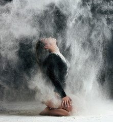 caucasian woman with long hair is dressed in a sports black bodysuit and sits on the floor and throwing white flour up