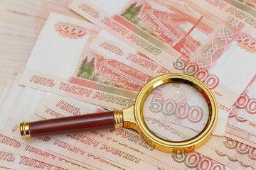 A magnifying glass with a gold handle is placed on top of Russian banknotes of five thousand rubles in large quantities