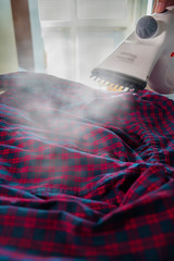 Iron with steamer for ironing a red shirt with a blue check.