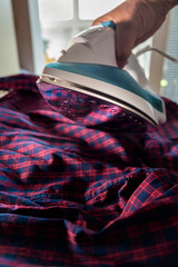 Iron with steamer for ironing a red shirt with a blue check.