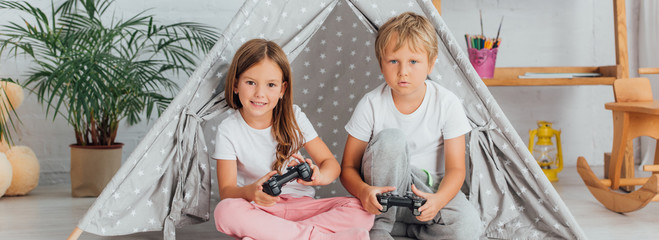 KYIV, UKRAINE - JULY 21, 2020: horizontal image of brother and sister in pajamas sitting on floor near kids wigwam and playing video game © LIGHTFIELD STUDIOS