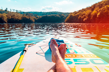 Men's feet on a paddleboard. First person view. Close-up of legs on surf. Relax and travel on the...
