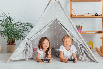 KYIV, UKRAINE - JULY 21, 2020:  brother and sister in pajamas lying on floor in kids wigwam and playing video game © LIGHTFIELD STUDIOS
