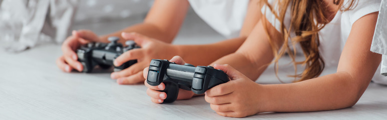KYIV, UKRAINE - JULY 21, 2020: cropped view of brother and sister lying on floor and playing video game with joysticks, horizontal image