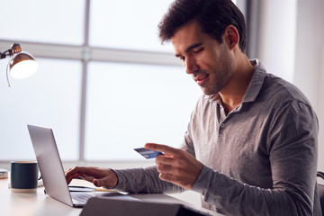 Businessman Working Late On Laptop At Desk In Office Making Online Payment With Credit Card