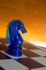 Board game chess. Figure of a transparent blue glass knight on a chessboard at an angle. The concept of falling, losing, rolling down.