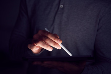 Close Up Of Businessman Working Late Drawing On Digital Tablet With Stylus Pen With Hand Illuminated