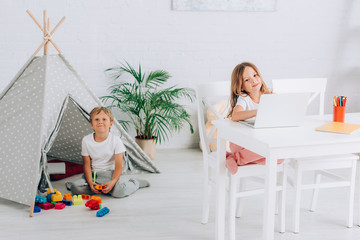 girl using laptop at table near brother sitting near kids wigwam and building blocks © LIGHTFIELD STUDIOS