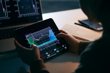 Close Up Of Female Share Trader At Desk With Stock Price Data Displayed On Laptop And Digital Tablet