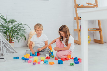 selective focus of children in pajamas sitting on floor and playing with building blocks