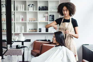 Young woman enjoying haircut at beauty salon with black master - obrazy, fototapety, plakaty