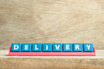 Tile letter on red rack in word delivery on wood background
