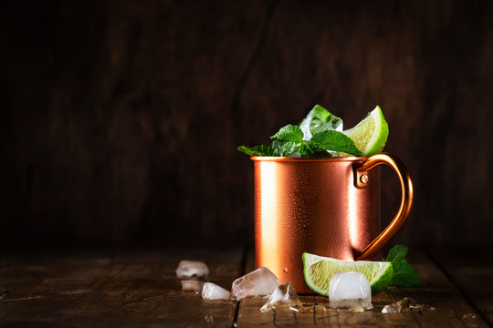 Moscow mule or mint julep cocktail in copper mug with lime, ginger beer, vodka and mint. Wooden table, copper bar tools,  copy space