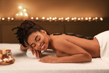Black young woman getting hot stone massage at spa