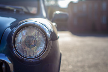 Close-up of a round headlight on an old car. On against the sun