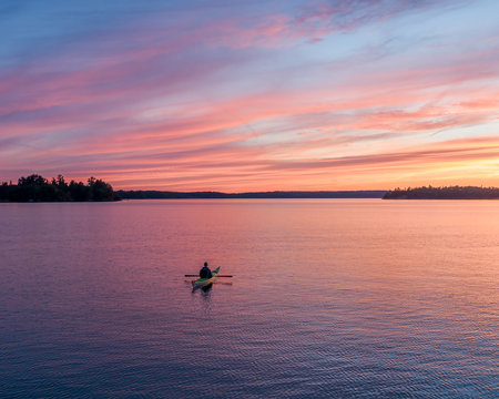 A Lone Kayaker Under A Colorful Sky At Sunset On A Lake In Northwest Ontario.