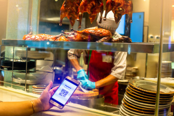 Selective focus to smartphone in hand to show QR code tag with blurry Chef chopping roast duck in in a Chinese restaurant to accepted generate digital pay without money. Qr code payment concept.