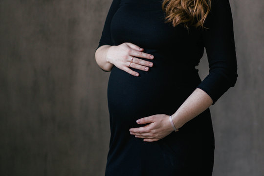 A Close-up Shot Of The Belly Of A 30 Weeks Pregnant Woman Wearing A Black Bodycon Dress. Going On Maternity Leave, Planning Pregnancy, Preparing For Childbirth