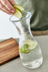 Person, die eine Wasser Karaffe mit Kräutern und geschnittenen Früchten befüllt