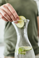 Person, die eine Wasser Karaffe mit Kräutern und geschnittenen Früchten befüllt