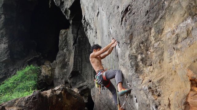From below of shirtless strong man training and climbing cliff in nature