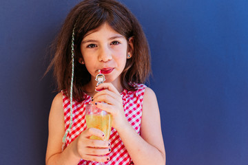 Little brunette girl drinkin orange juice with a straw. Copy space
