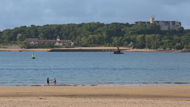 People walking along Somo beach with the Magdalena palace in the background. Santander, Cantabria
