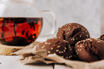 Teapot with black tea and homemade chocolate cookies on a white natural wooden background