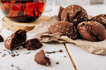 Teapot with black tea and homemade chocolate cookies on a white natural wooden background