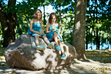 two cute little girls in dresses sit on a stone and drink lemonade 