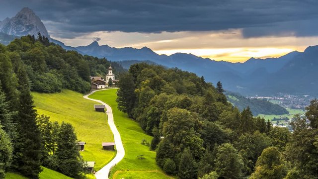 Summer time alps mountain nature panoramic landscape near garmisch partenkirchen bavaria germany in backgorun alps mountain in front of church time lapse video in 4k. alpine meadow.