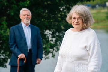 Portrait of a cheerful Caucasian elderly man and woman standing in nature against the backdrop of the lake