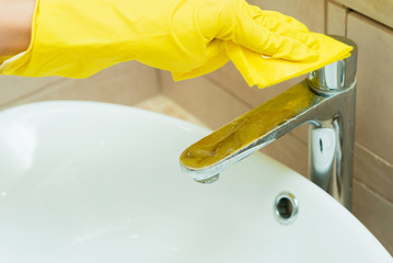 Someone is washing a sink in yellow gloves. Someone is cleaning a bathroom with detergents