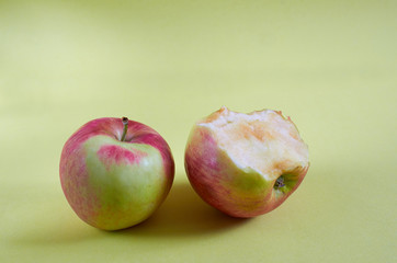 A whole Apple and a bitten Apple lie on a colored background
