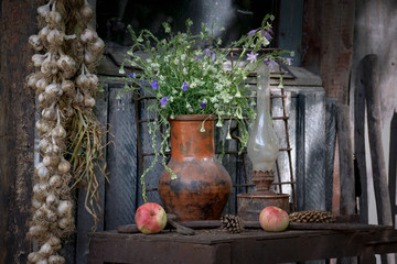 Obraz premium Still life in vintage style, a clay pot with flowers and an old rusty lamp on a shabby stand.