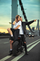 Fototapeta na wymiar Biker man and girl stands on the road and looks into the distance. Love and romantic concept