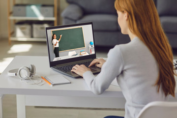 Online education. Young girl sitting at the table at home using laptop for online lesson. Distance learning in college, school.