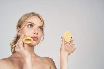 A blonde with bare shoulders holds cotton pads near her face skin care light background