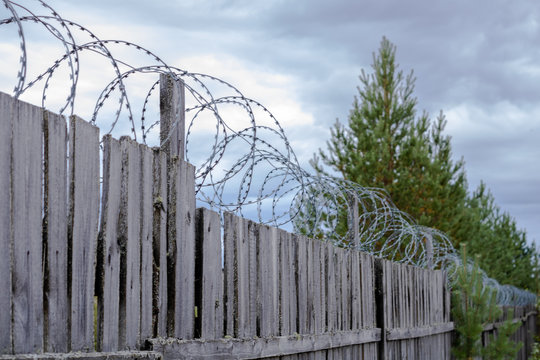 Wooden fence with barbed wire on the background of the cloudy sky.