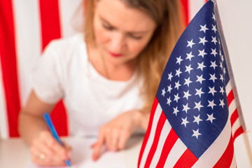 The American woman fills out the documents. The girl writes against the background of the American flag. Immigration to the USA. Elections in America. Filling out a ballot for voting in US elections.