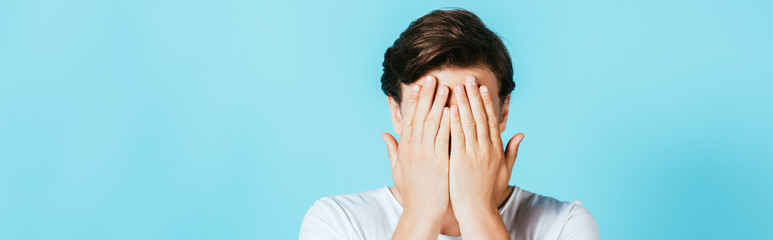 Panoramic shot of man covering face with hands on blue background