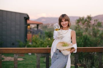 Young beautiful woman drinking wine in winery at sunset on summer sunny day.