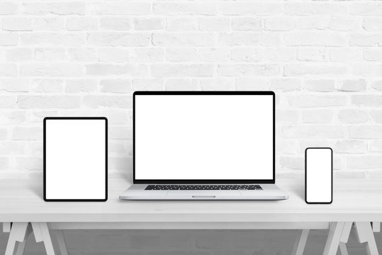 Devices with isolated screens for responsive web design promotion. Web design studio concept on white wooden desk and brick wall in background