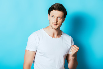 Angry man in white t-shirt showing fist on blue background