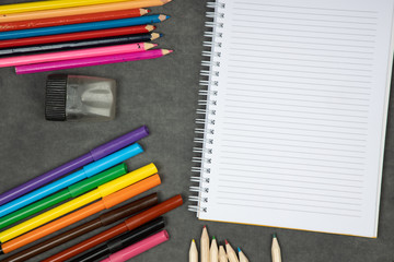 Obraz premium Colorful school supplies on blackboard. Blank notepad with various pencils, markers and crayons. Back to school concept.