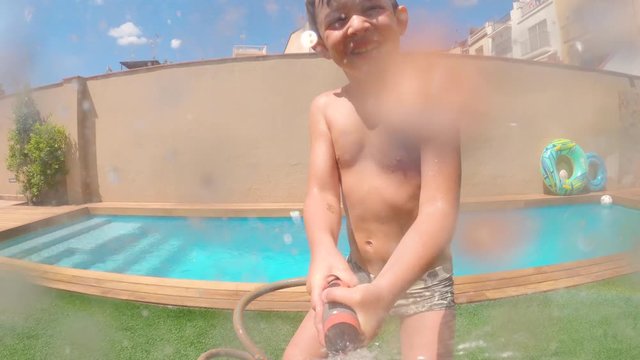 Happy five-year-old boy plays to wet the camera that is recording him. Having fun in a sunny day.