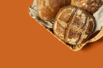 Homemade freshly baked bread lies in a wicker basket on an orange uniform background. Bakery - crusty loaves of bread. Layout with free copy  space.Bread background - top view, flat lay