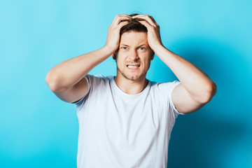 Young angry man in white t-shirt looking at camera on blue background