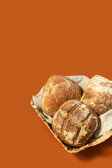 Homemade freshly baked bread lies in a wicker basket on an orange uniform background. Bakery - crusty loaves of bread. Layout with free copy  space.Bread background - top view, flat lay