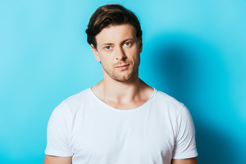 Confident man in white t-shirt looking at camera on blue background